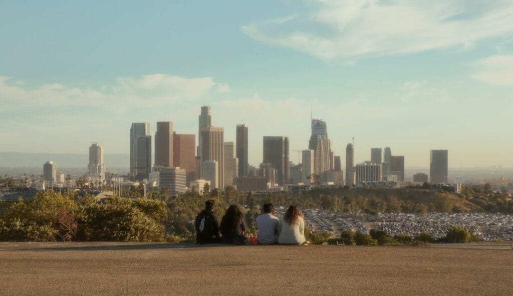 Hikers enjoying a view of Downtown Los Angeles from a scenic overlook, with downtown skyscrapers and urban landscape in the background.